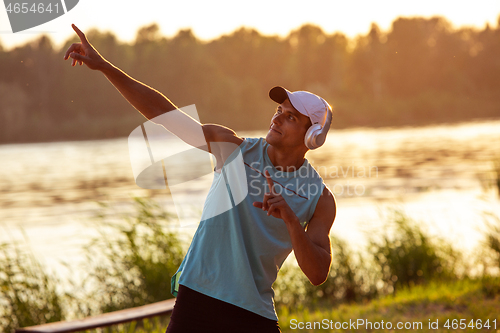 Image of A young athletic man working out listening to the music at the riverside outdoors