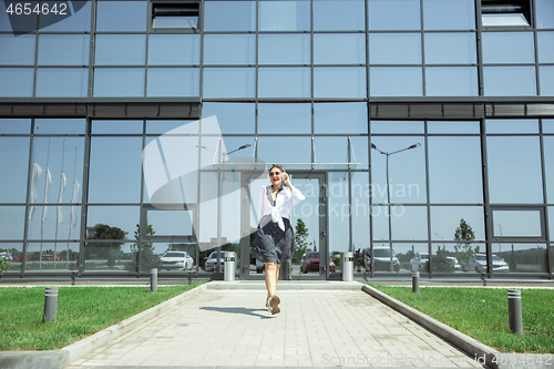 Image of Young woman walking against glass\' wall in airport, traveler with small baggage, influencer\'s lifestyle