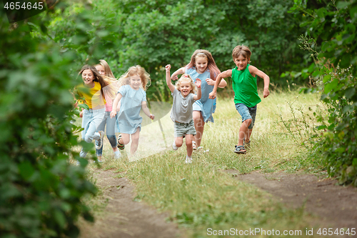 Image of Kids, children running on green meadow, forest. Childhood and summertime