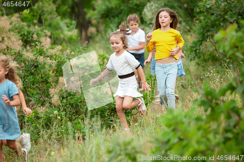 Image of Kids, children running on green meadow, forest. Childhood and summertime