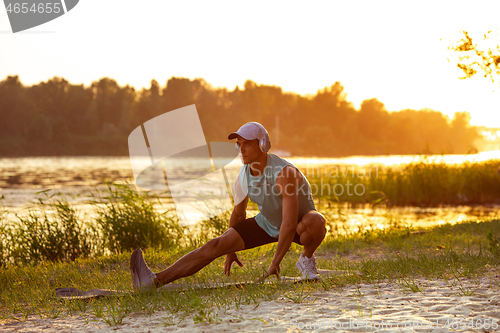 Image of A young athletic man working out listening to the music at the riverside outdoors