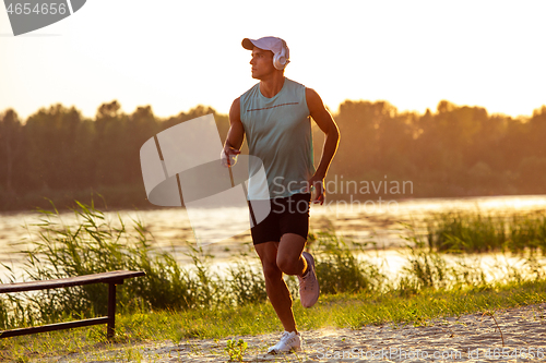 Image of A young athletic man working out listening to the music at the riverside outdoors