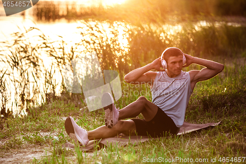 Image of A young athletic man working out listening to the music at the riverside outdoors