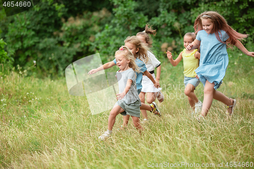 Image of Kids, children running on green meadow, forest. Childhood and summertime