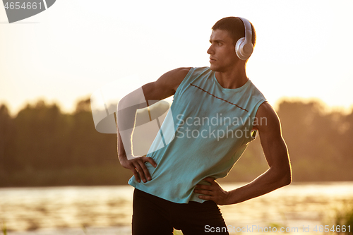 Image of A young athletic man working out listening to the music at the riverside outdoors