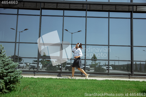 Image of Young woman walking against glass\' wall in airport, traveler with small baggage, influencer\'s lifestyle