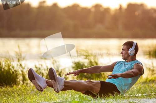 Image of A young athletic man working out listening to the music at the riverside outdoors