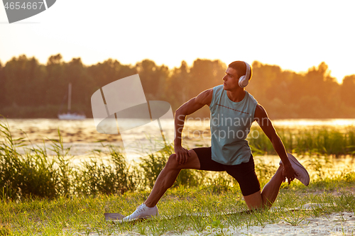 Image of A young athletic man working out listening to the music at the riverside outdoors