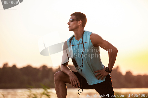 Image of A young athletic man working out listening to the music at the riverside outdoors