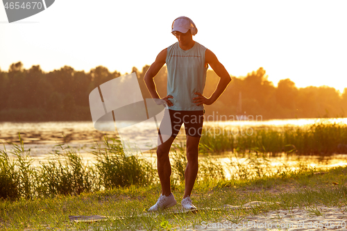 Image of A young athletic man working out listening to the music at the riverside outdoors