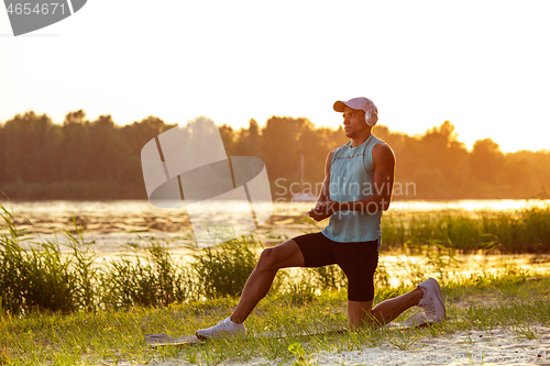 Image of A young athletic man working out listening to the music at the riverside outdoors