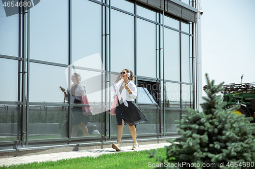 Image of Young woman walking against glass\' wall in airport, traveler with small baggage, influencer\'s lifestyle