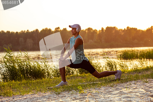 Image of A young athletic man working out listening to the music at the riverside outdoors