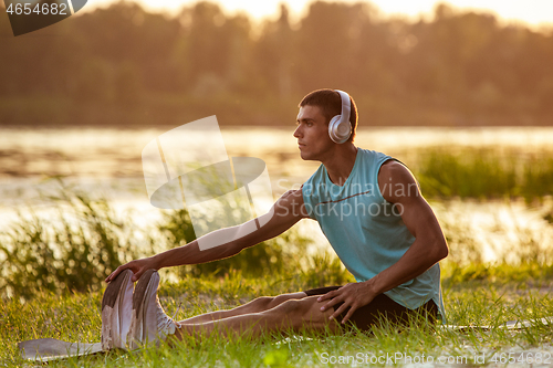 Image of A young athletic man working out listening to the music at the riverside outdoors