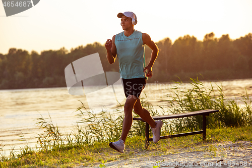 Image of A young athletic man working out listening to the music at the riverside outdoors