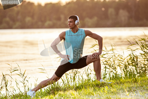 Image of A young athletic man working out listening to the music at the riverside outdoors