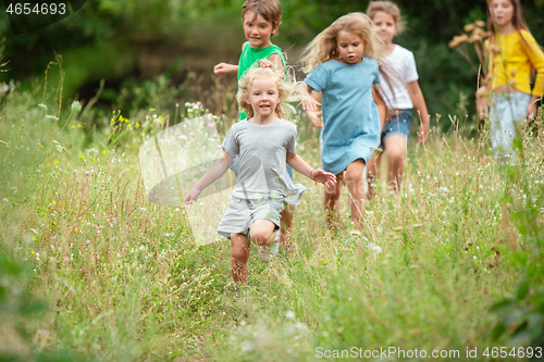 Image of Kids, children running on green meadow, forest. Childhood and summertime