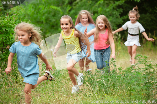 Image of Kids, children running on green meadow, forest. Childhood and summertime