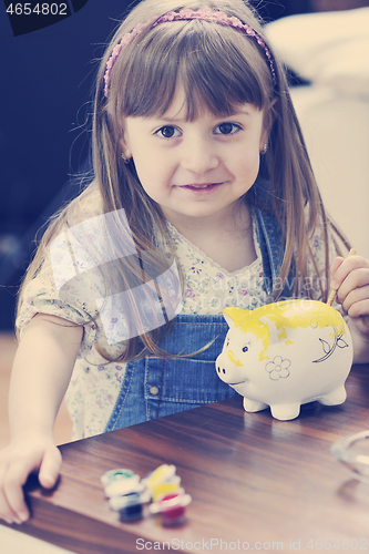 Image of cute little girl painting piggy bank