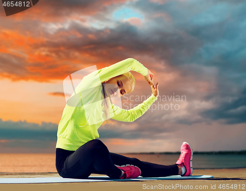 Image of woman stretching on exercise mat at seaside