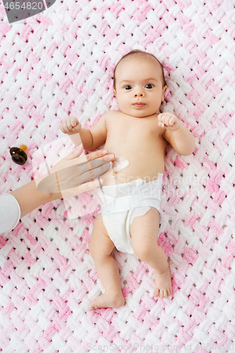 Image of hand applying body lotion to baby girl\'s tummy