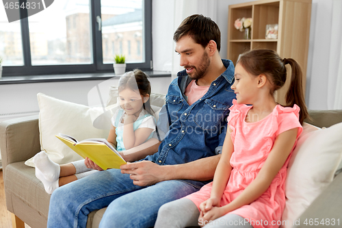 Image of happy father with daughters reading book at home