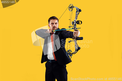 Image of Businessman aiming at target with bow and arrow, isolated on yellow background