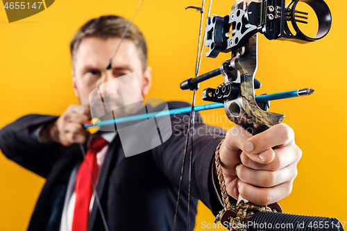 Image of Businessman aiming at target with bow and arrow, isolated on yellow background