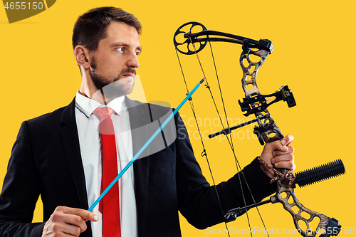 Image of Businessman aiming at target with bow and arrow, isolated on yellow background