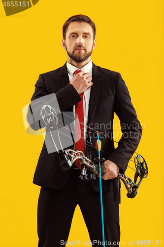 Image of Businessman aiming at target with bow and arrow, isolated on yellow background