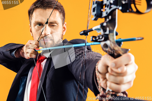 Image of Businessman aiming at target with bow and arrow, isolated on yellow background