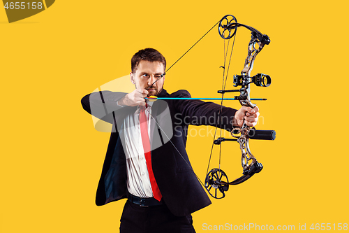 Image of Businessman aiming at target with bow and arrow, isolated on yellow background