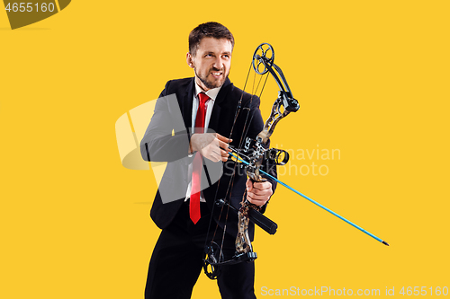 Image of Businessman aiming at target with bow and arrow, isolated on yellow background