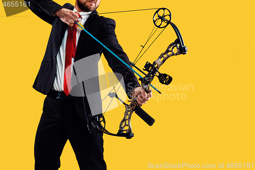 Image of Businessman aiming at target with bow and arrow, isolated on yellow background