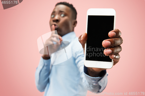 Image of Indoor portrait of attractive young black man holding blank smartphone