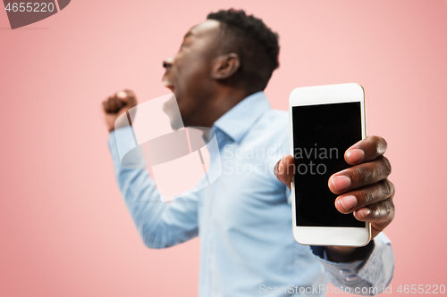 Image of Indoor portrait of attractive young black man holding blank smartphone