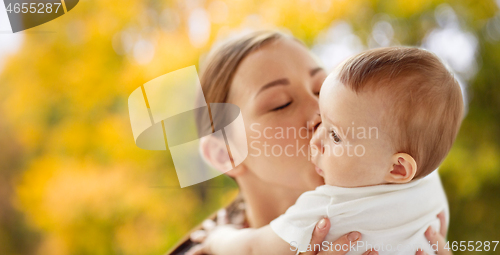 Image of happy young mother kissing little baby in autumn