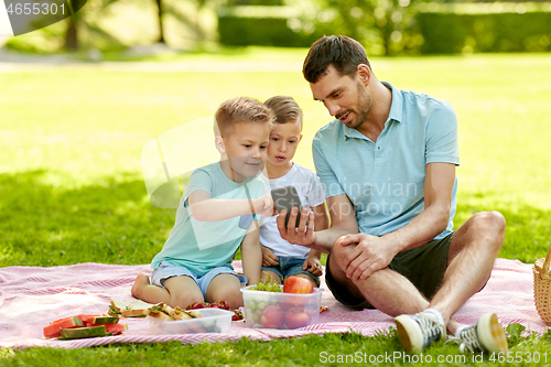 Image of family with smartphone having picnic at park