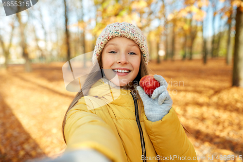 Image of happy girl with apple taking selfie at autumn park