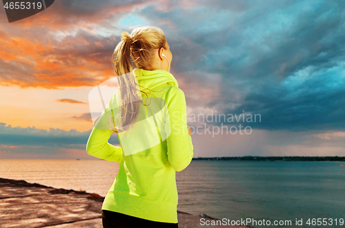 Image of woman with earphones running over sea sunset