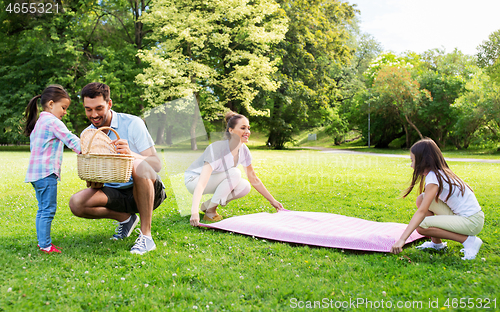 Image of family laying down picnic blanket in summer park