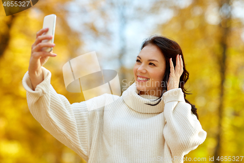 Image of woman taking selfie by smartphone at autumn park