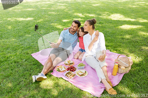 Image of family having picnic and taking selfie at park