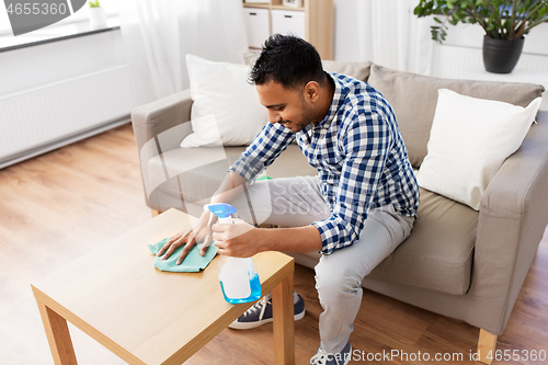 Image of indian man cleaning table with detergent at home