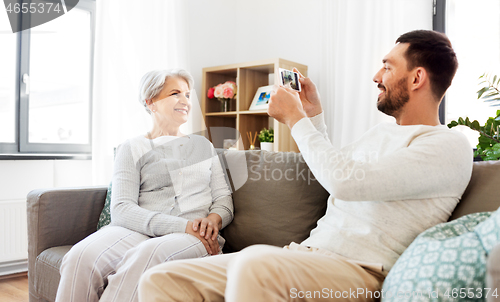 Image of adult son photographing senior mother at home