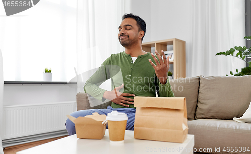 Image of pleased indian man eating takeaway food at home