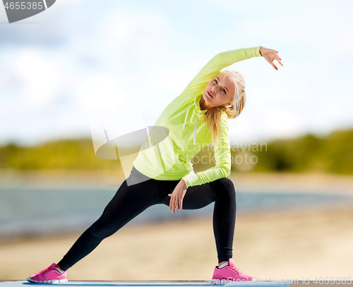 Image of woman stretching on exercise mat on beach