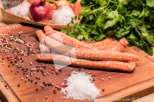 Image of raw sausages with chilli and herbs on a wooden board with spices