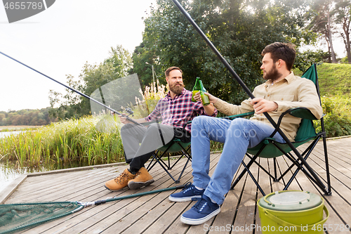 Image of happy friends fishing and drinking beer on pier