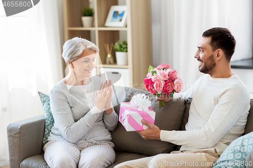 Image of son giving present and flowers to senior mother